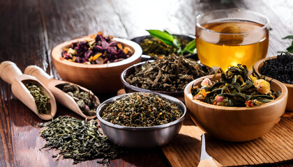 Wall Mural - A variety of dried tea leaves and herbal infusions displayed in wooden bowls on a rustic table. The image conveys natural warmth and the concept of healthy relaxation.