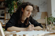 © Marut - A focused designer is sketching sustainable project, surrounded by wooden models and plants, showcasing creativity and dedication in her workspace