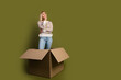 © deagreez - Young woman in knitwear pondering standing in an open cardboard box on a khaki background