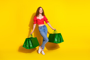 Full body photo of attractive young woman look empty space hold shopping bags dressed red clothes isolated on yellow color background