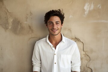 Portrait of a content man in his 20s wearing a simple cotton shirt on bare concrete or plaster wall