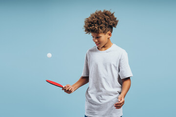 Portrait of positive happy African American boy, teenager playing ping pong, holding racket and ball