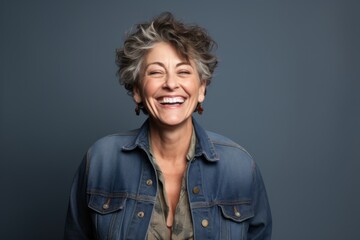 Wall Mural - Portrait of a joyful woman in her 50s wearing a rugged jean vest over blank studio backdrop