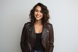 © Markus Schröder - Portrait of a joyful indian woman in her 20s sporting a classic leather jacket isolated on light wood minimalistic setup