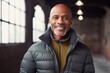 © Markus Schröder - Portrait of a satisfied afro-american man in his 50s sporting a quilted insulated jacket while standing against empty modern loft background
