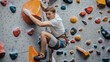 © Alfazet Chronicles - Young man climbing indoor rock wall with safety harness and colorful holds in a climbing gym.