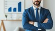 © Nitchalee N. - A professional man in a blue suit stands confidently with crossed arms, in front of a chart depicting growth in a modern office setting.