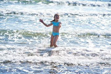 Wall Mural - An 8 year old girl in a swimsuit having fun in the sea waves.