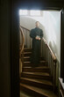 © AnnaStills - Vertical shot of young priest holding Bible in black cover standing on spiral wooden stair while posing for portrait