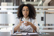 © Tetiana - A young African American female doctor in a white coat and glasses is sitting at a desk in a hospital office, talking and consulting at the camera while gesturing with her hands