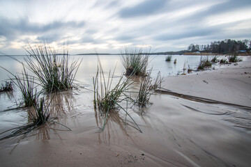 Wall Mural - Sunrise over a lake in autumn. A wooden jetty protrudes into the water while grass has established itself on the sandy beach. The lake and beach, located on Lake Vänern in Näs Sannar, Sweden, Scandina