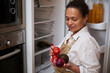 © Taras Grebinets - Woman in apron selecting fresh produce from refrigerator
