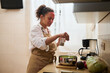 © Taras Grebinets - Woman wearing an apron preparing a meal in a cozy kitchen, adding spices to a bowl of vegetables, creating a sense of home cooking, warmth, and culinary creativity in a casual setting.