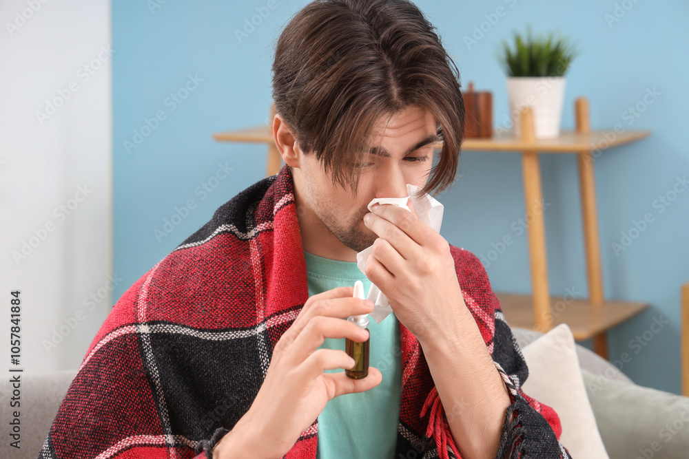 Sick young man with nasal drops and tissue sneezing at home, closeup