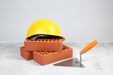 Red bricks, trowel and hard hat on textured table against light background