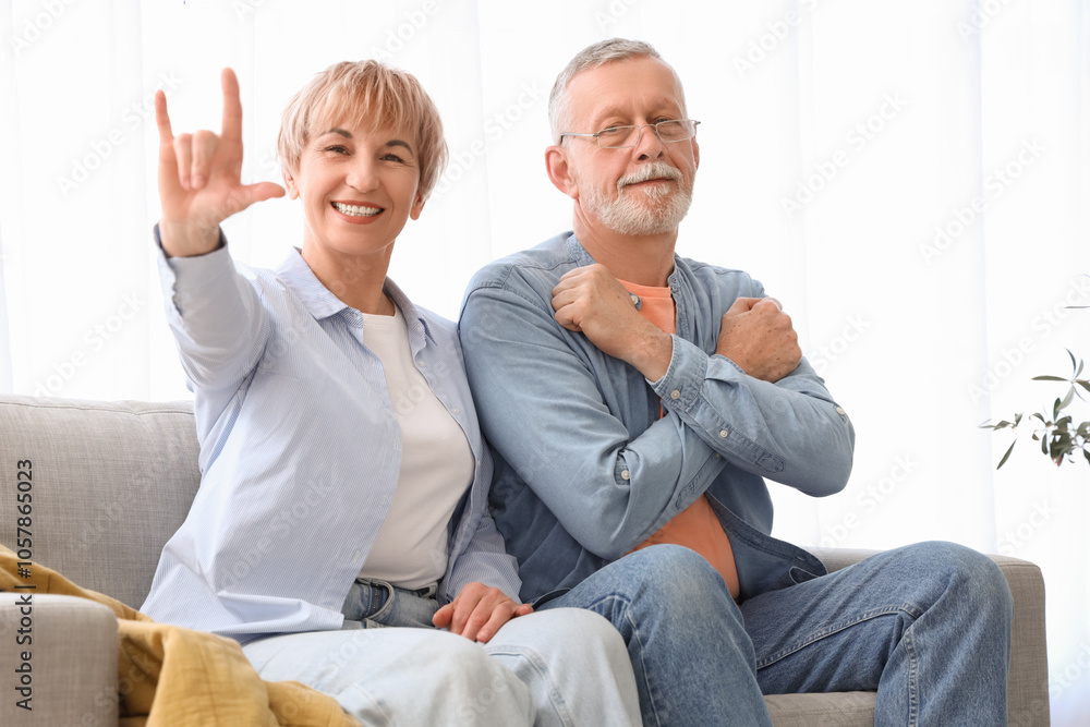 Mature deaf mute couple using sign language on sofa at home