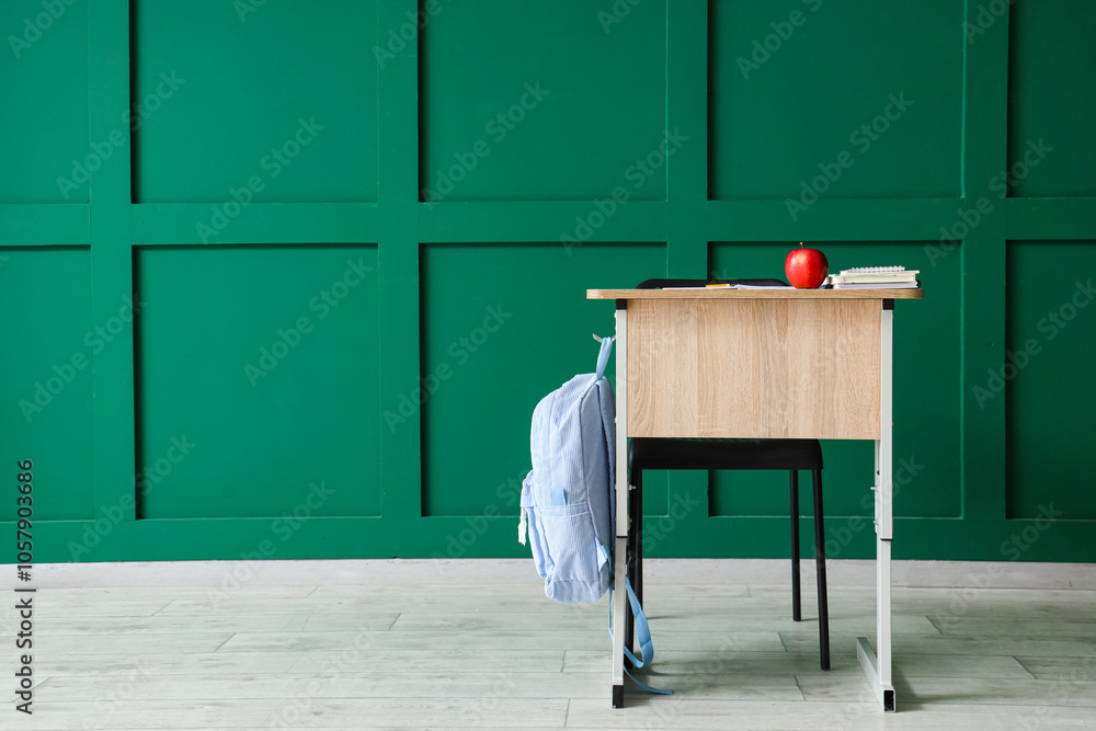 School desk with books and apple near green wall