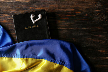 Holy Bible, earphones and flag of Ukraine on wooden background