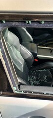 Naples, Italy - December 23, 2023: Front right window of a silver Range Rover Evoque shattered, with glass fragments scattered on the black leather seats