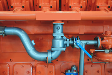 Poster - Large orange piston gas engine electric generator with many valves and pipes. The engine is orange and has many valves.