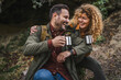 © Miljan Živković - husband and wife hikers sit in front cave and drink from metal mug