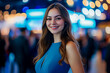 © Saulo Studio - Beautiful young woman in a blue dress smiling at the camera, posing at the business event conference, screens and blurred crowd.