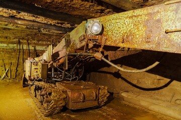 This photo shows a dark and grungy mine shaft with a single light illuminating the foreground. The walls of the shaft show signs of wear and tear, and the air is thick with dust and debris.