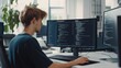 © Aris Suwanmalee - A young programmer working at a modern desk, focused on coding tasks on dual computer monitors in a bright office environment.