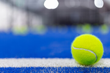 Bright yellow tennis ball resting on a blue court with blurred background during an indoor match capture