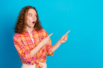 Surprised young woman in casual plaid shirt pointing sideways against a vibrant blue background