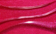 © Magnus Cramer - Red shimmering lip gloss texture background. Smudged cosmetic product smear. Makup swatch product sample