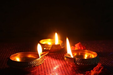 Diwali celebration. Diya lamps and beautiful flowers on dark background, closeup