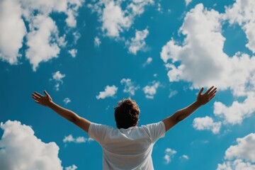 A person stands with arms outstretched against a vibrant blue sky filled with fluffy white clouds, symbolizing freedom, hope, and a connection with nature.