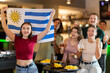 © JackF - Group of friends fans watching match cheering with Uruguayan flag in bar
