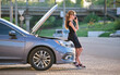 © bilanol - Helpless woman standing near her car with open hood takling on mobile phone calling road service for help. Young female driver having trouble with vehicle