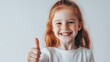 © Pixcellence - Smiling Little Girl with Red Hair and Freckles Giving Thumbs Up