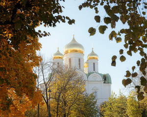 Cathedral of St. Catherine glowing in bright sunlight, surrounded by autumn trees with yellowing leaves, creating a picturesque scene.