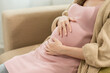 © Chanakon - Happy pregnant woman caresses her belly while taking rest on sofa at home, concept of happy motherhood waiting for childbirth, family planning and pregnancy with insurance for child health.