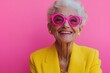 © Vooglo.com - A joyful elderly woman wearing bold pink sunglasses and a vibrant yellow jacket stands