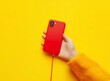 © munja02 - Close-up of a child's hand holding a red phone with a cable on a yellow background
