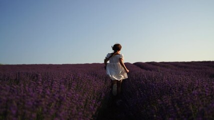 Wall Mural - Girl is runs through a field of purple flowers. She is wearing a white shirt and a hat.