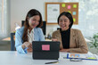 © crizzystudio - Two young businesswomen pointing to plans, statistics, and data graphs and explaining the conditions of their partnership, happily acknowledging their turnover and income during negotiations.