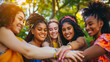 © Mahemud - A multicultural group of women stack hands together, symbolizing female community support with different girls hugging outdoors.