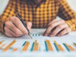 © Preeyanuch - A close-up of a business professional analyzing data on a chart with a pen, showcasing analytical skills and attention to detail.