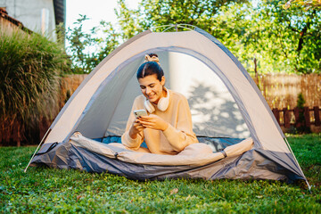 young woman listening to music or audio book in tent in backyard