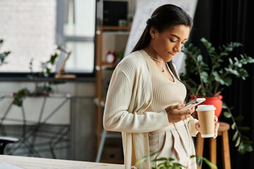 A young woman enjoys coffee while looking at her phone in a modern office.