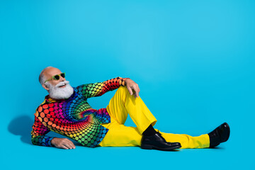 Full length photo of eccentric funky aged man sitting floor empty space isolated on blue color background