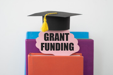 The concept of business financing and grants. GRANT FUNDING on the card against the background of textbooks