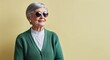 © Arceli - Gray Haired Elderly Woman with Neat Short Hair in Green Cardigan and Sunglasses on Light Yellow Background