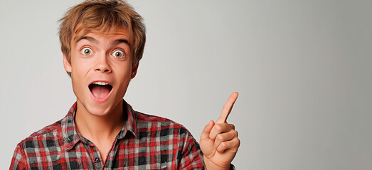 Surprised young man pointing excitedly to side for attention. Happy man in plaid shirt pointing at empty space for text.